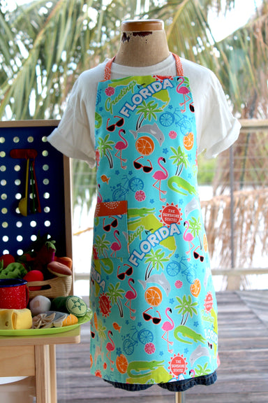 Greetings From Florida Kid's Apron-The Blue Peony-Age Group_Kids,Animal_Aligator,Animal_Dolphin,Animal_Flamingo,Category_Apron,Color_Aqua,Department_Kitchen,Gender_Boys,Gender_Girls,Material_Cotton,Size_Medium (ages 6-11),Size_Small (ages up to 5),Theme_Animal,Theme_Tropical,Theme_Water Life